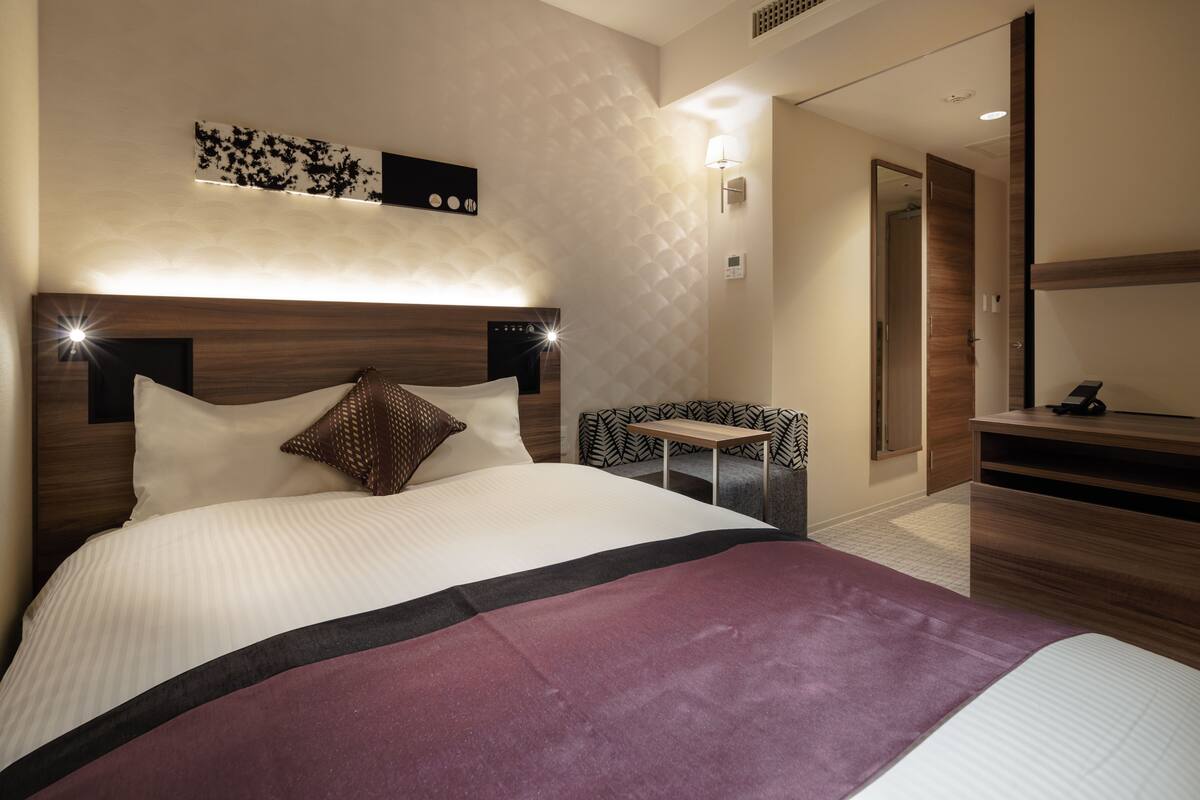 Una habitación de hotel moderna con una cama grande, una mesita de noche, un escritorio pequeño y un espejo.