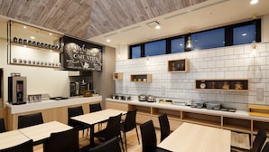 Un café moderno con mesas y sillas de madera, una máquina de café y estanterías con frascos y utensilios de cocina.