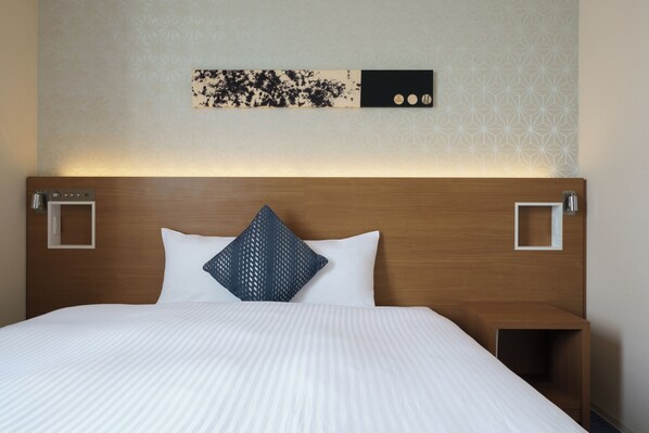 Une chambre d’hôtel avec une tête de lit en bois, du linge de lit blanc, un élément décoratif mural et une petite table de chevet avec une lampe.