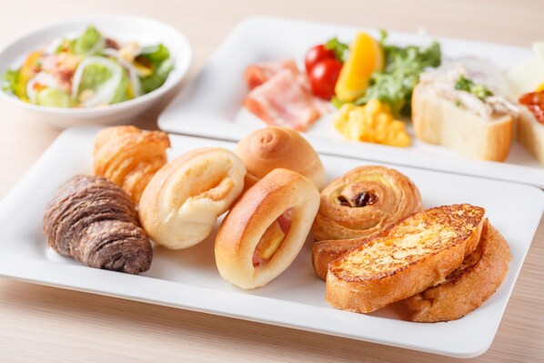 Une assiette de petit-déjeuner avec des croissants, un pain au jambon et des toasts.