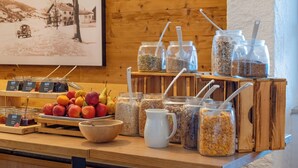 Een ontbijtbuffet met fruit, granen en een oud schilderij op de achtergrond.