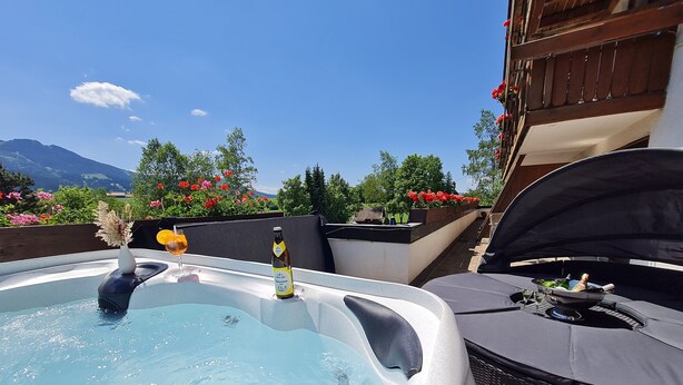 Een jacuzzi met een biertje en een glas bier, omringd door tuinmeubilair en een barbecue.