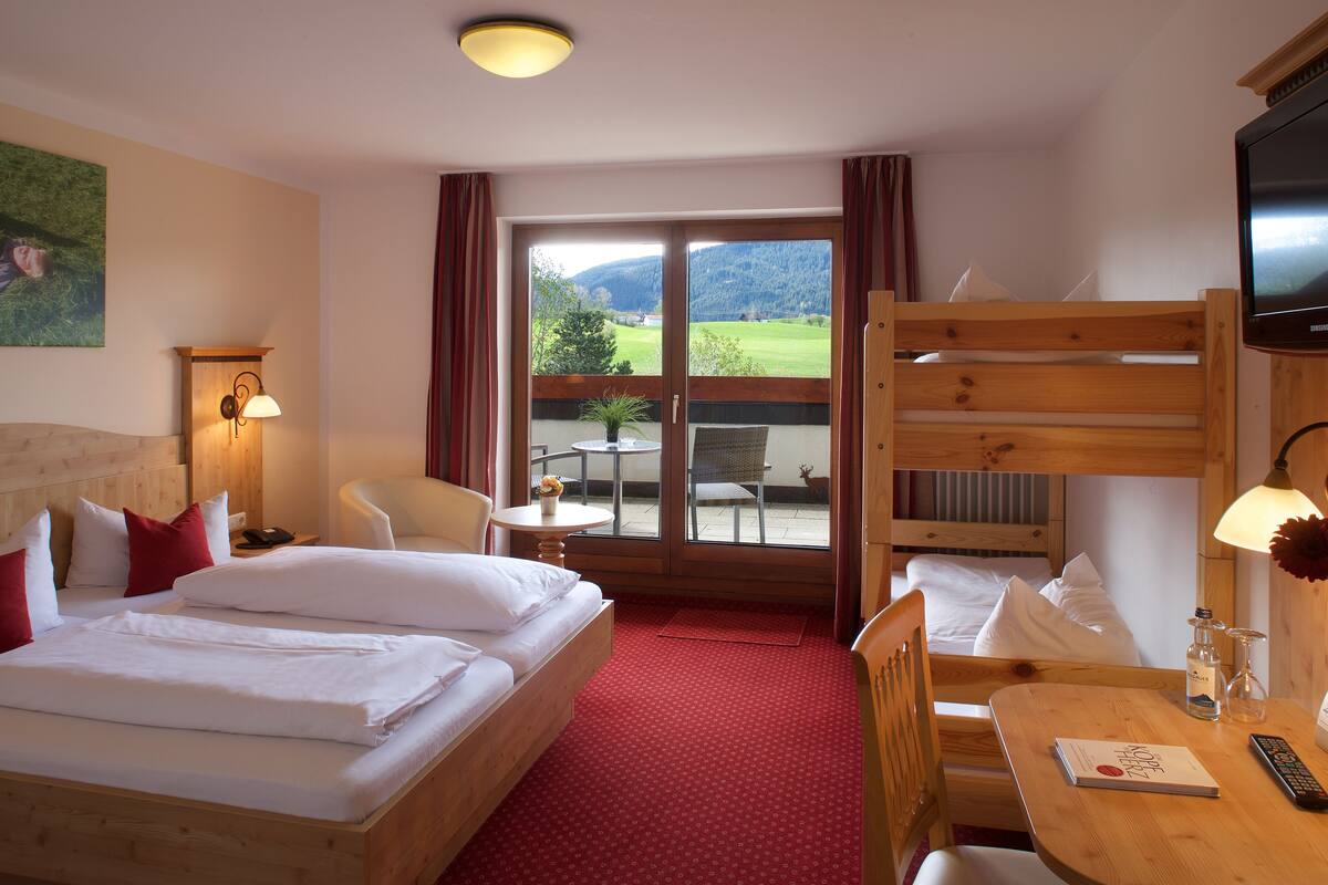 Une chambre d’hôtel avec deux lits, un bureau, une chaise, une télévision et un balcon offrant une vue sur les montagnes.