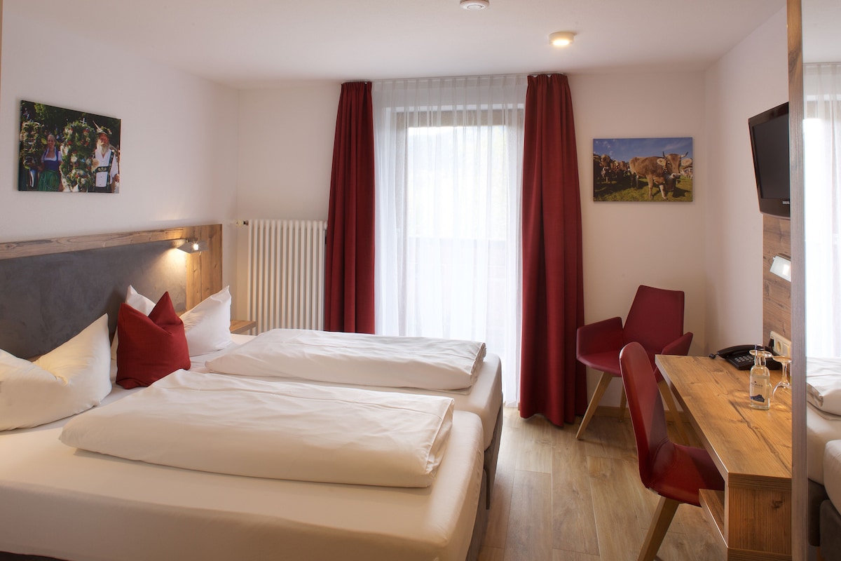 Een hotelkamer met twee bedden, een houten tafel, een stoel, een televisie en kunst aan de muren.