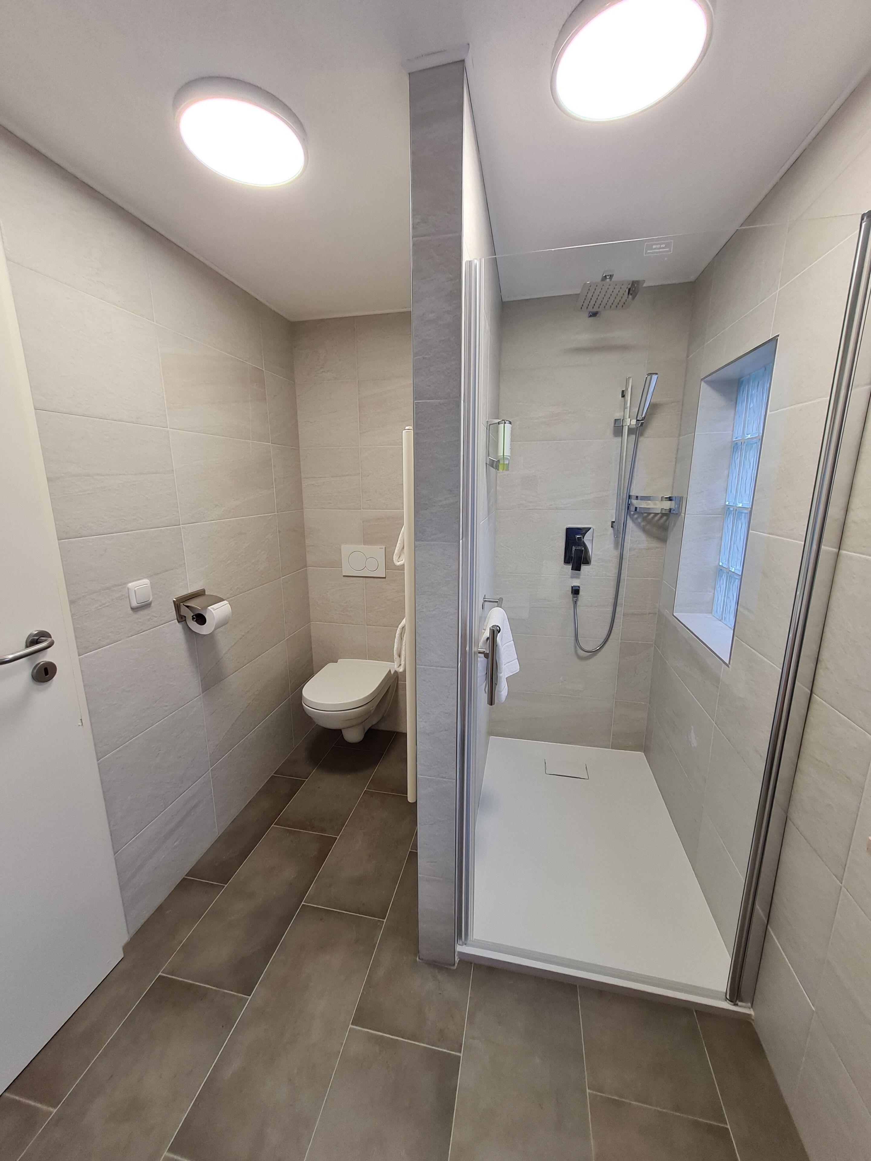 Un baño moderno con ducha envuelta en vidrio, inodoro y perchero.