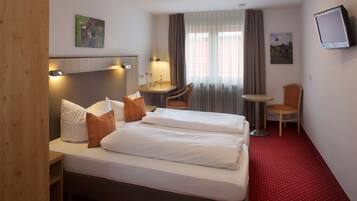 A hotel room with a bed, a desk, a chair, a TV, and a window with curtains.