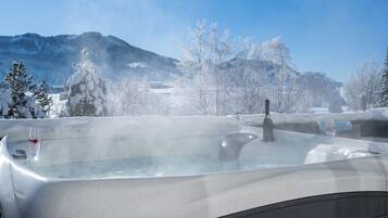 A hot tub with a glass of wine, surrounded by snow-covered trees and mountains.