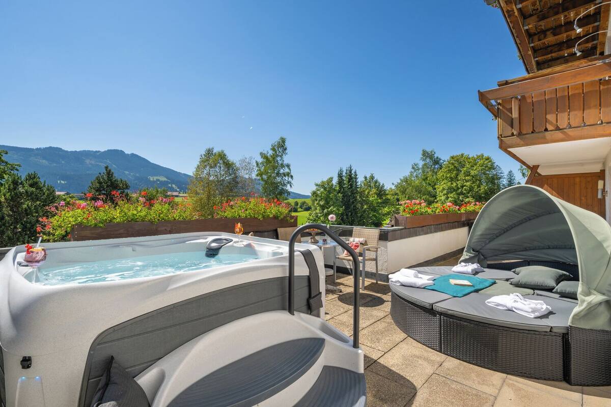 Un bain à remous avec vue sur les montagnes, un espace salon couvert et une terrasse en bois.
