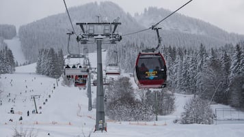 A ski lift with a red chair carrying passengers, surrounded by snow-covered trees and a snowy mountain in the background.