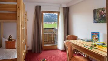 A room with a bunk bed, a wooden desk, a chair, a window with curtains, and a view of mountains.