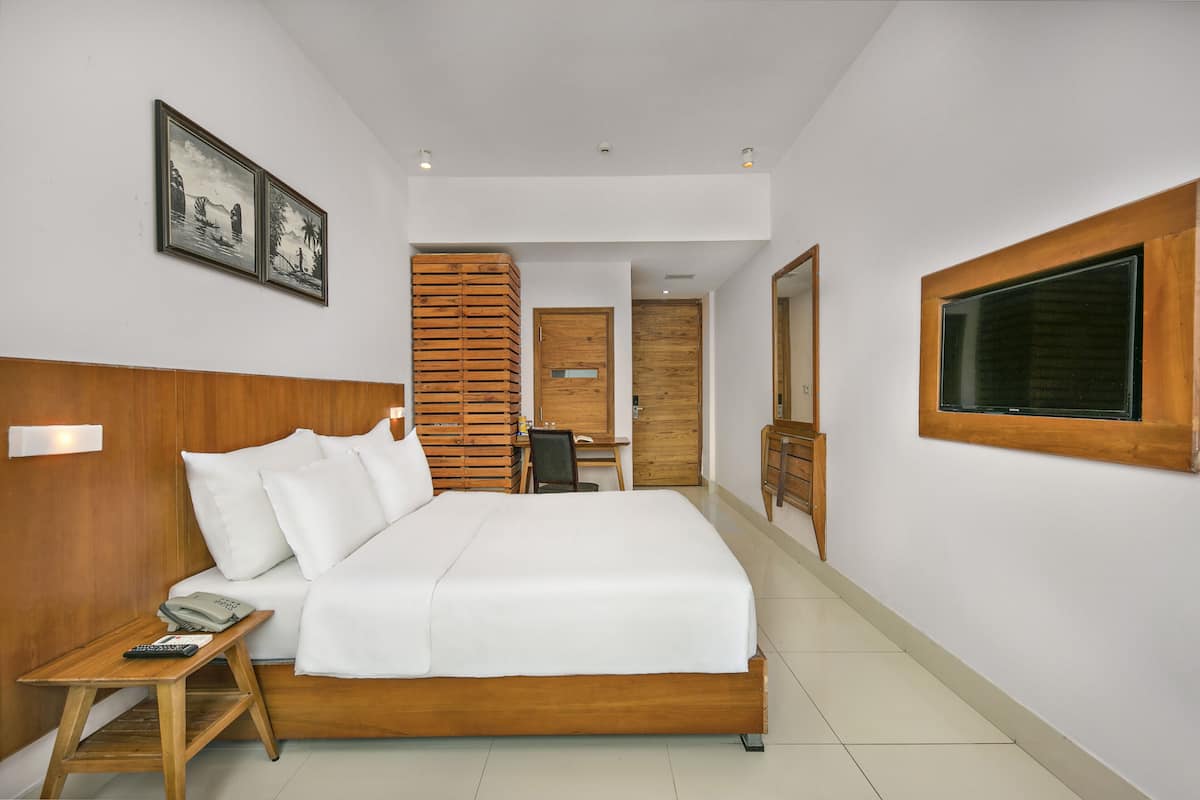Quarto de hotel com cama de madeira, uma escrivaninha, uma cadeira e uma janela grande.