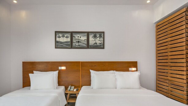 A hotel room with two beds, wooden headboard, white bedding, a nightstand with a phone and remote, and wall-mounted artwork. - Da Nang Bay Hotel (Da Nang)