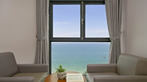 A room with a large window, two sofas, a small table with a plant and a book, and a view of the sea. - Da Nang Bay Hotel (Da Nang)