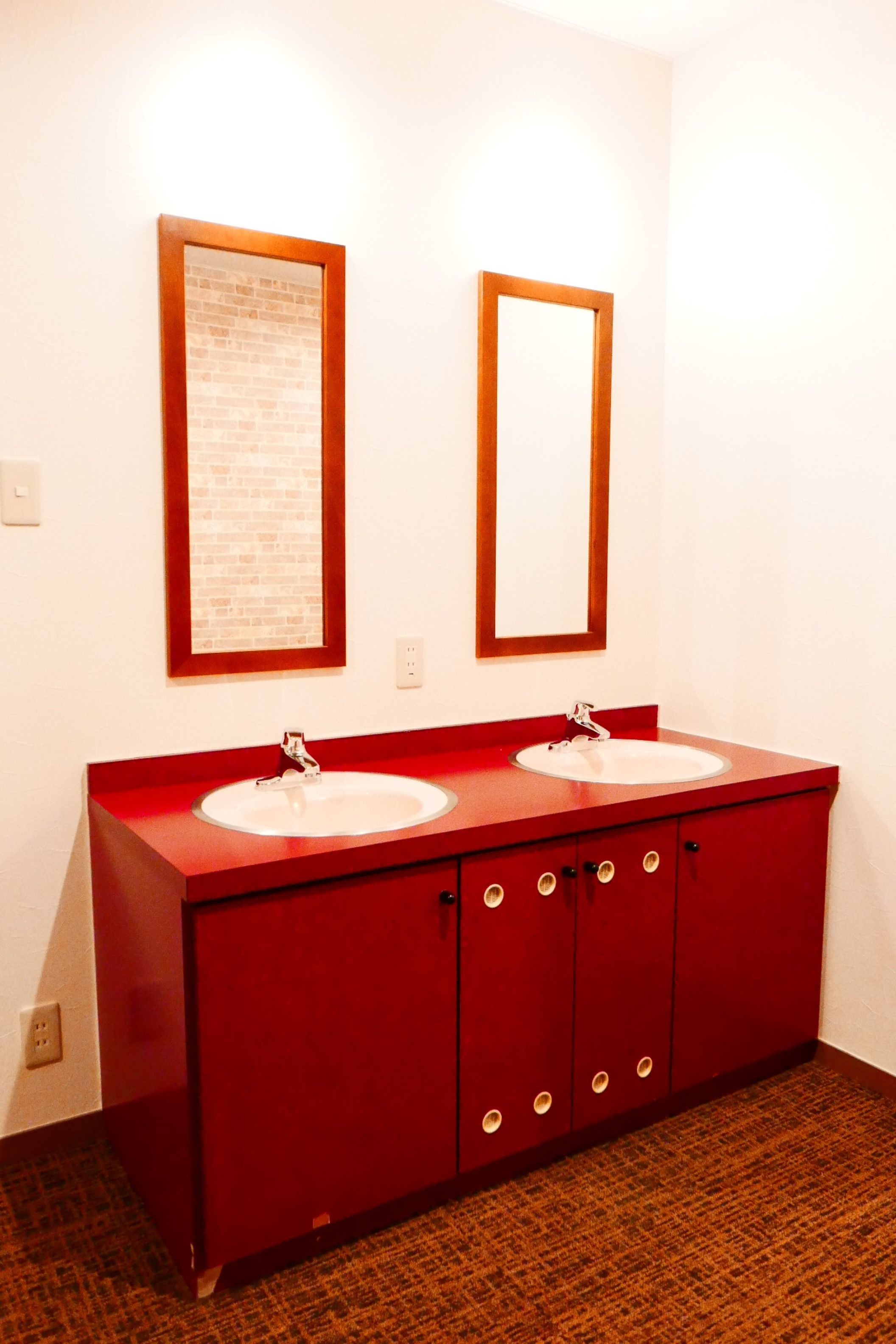 A red bathroom vanity with two sinks and a mirror above each.