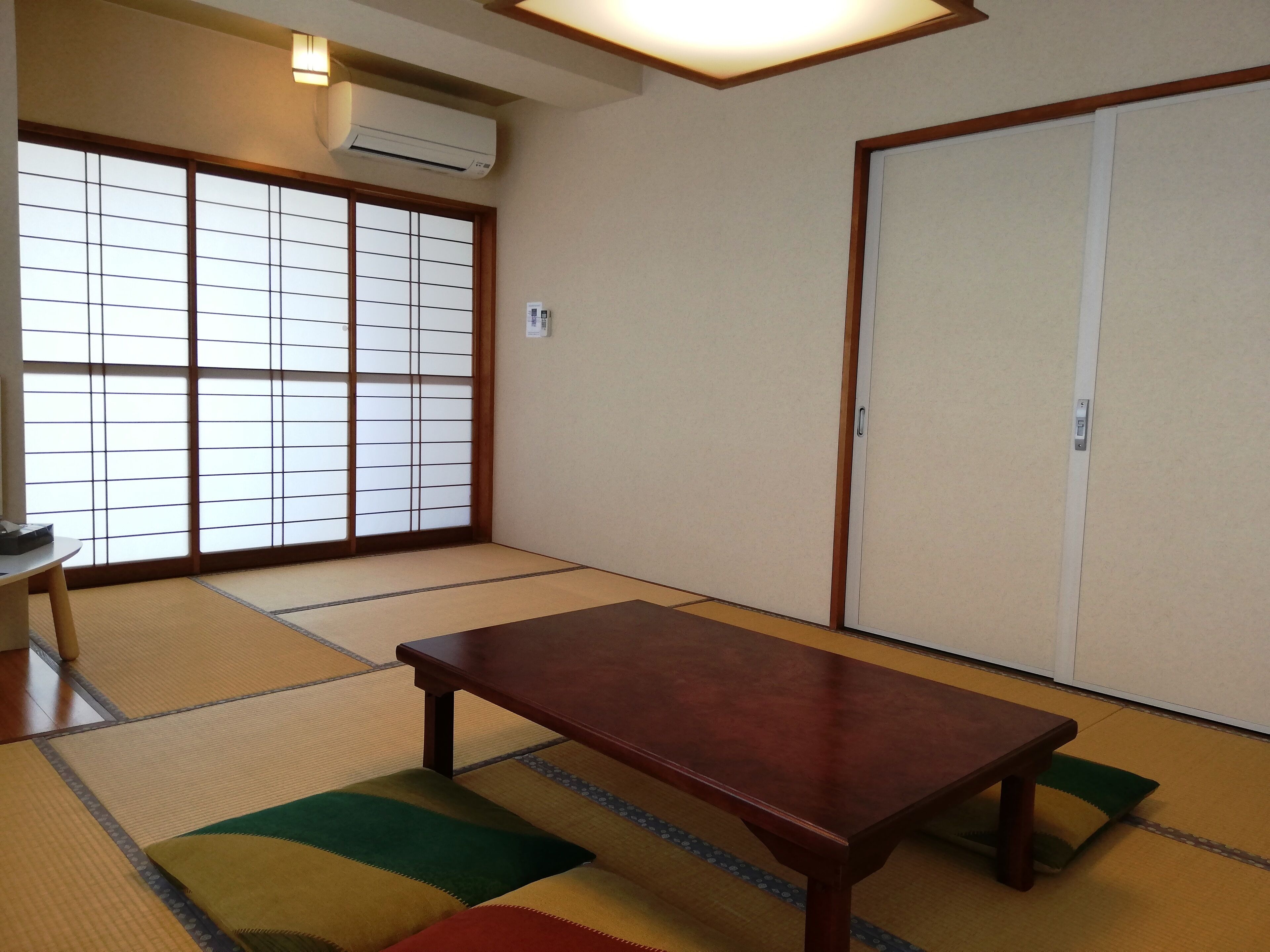 Una habitación tradicional japonesa con suelo de tatami, una mesa de madera, puertas correderas y un aire acondicionado instalado en el techo.