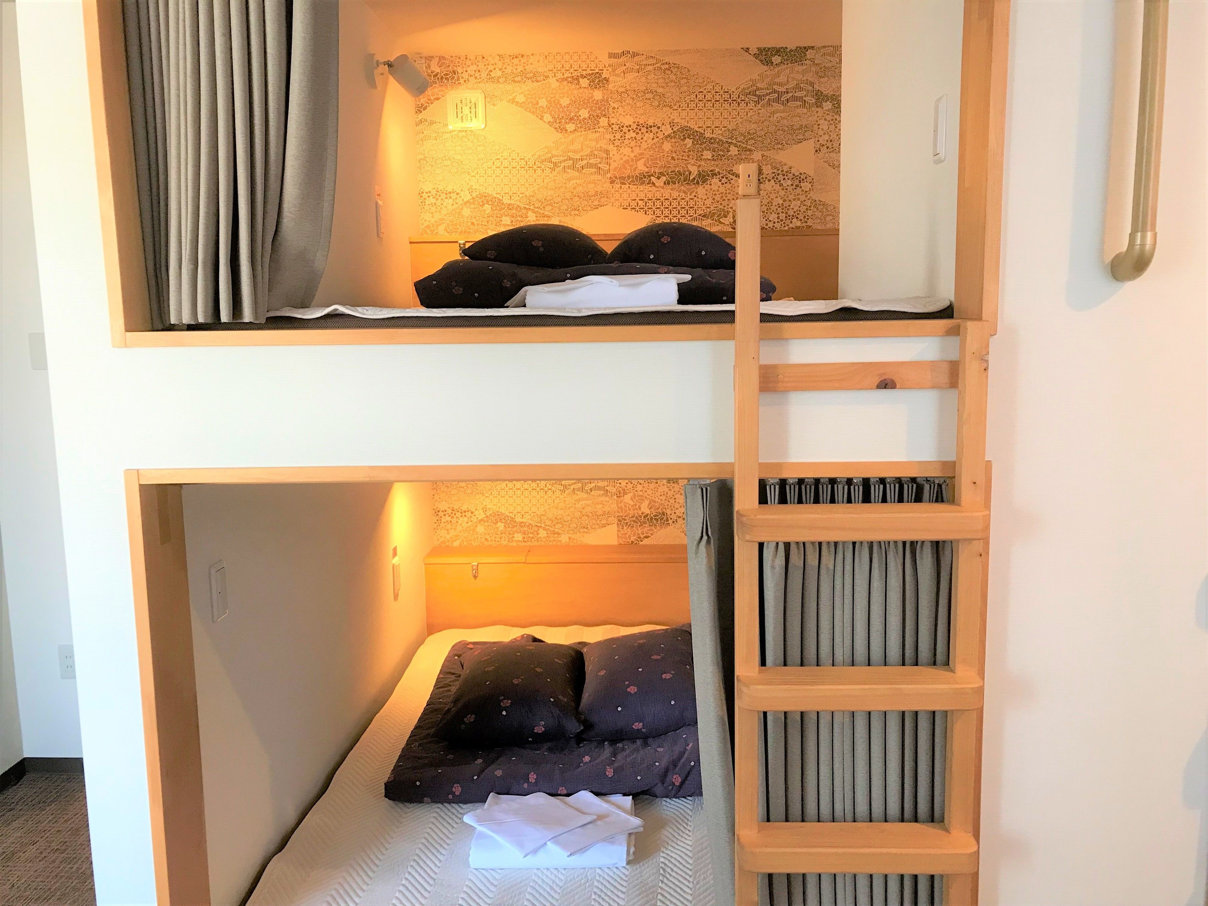 Dormitorio con literas, una escalera, una luz fijada a la pared y un tapiz estampado.