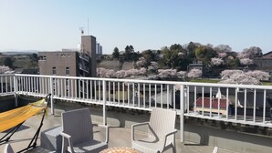 A balcony with a yellow hammock, white wicker chairs, and a small tiled table.