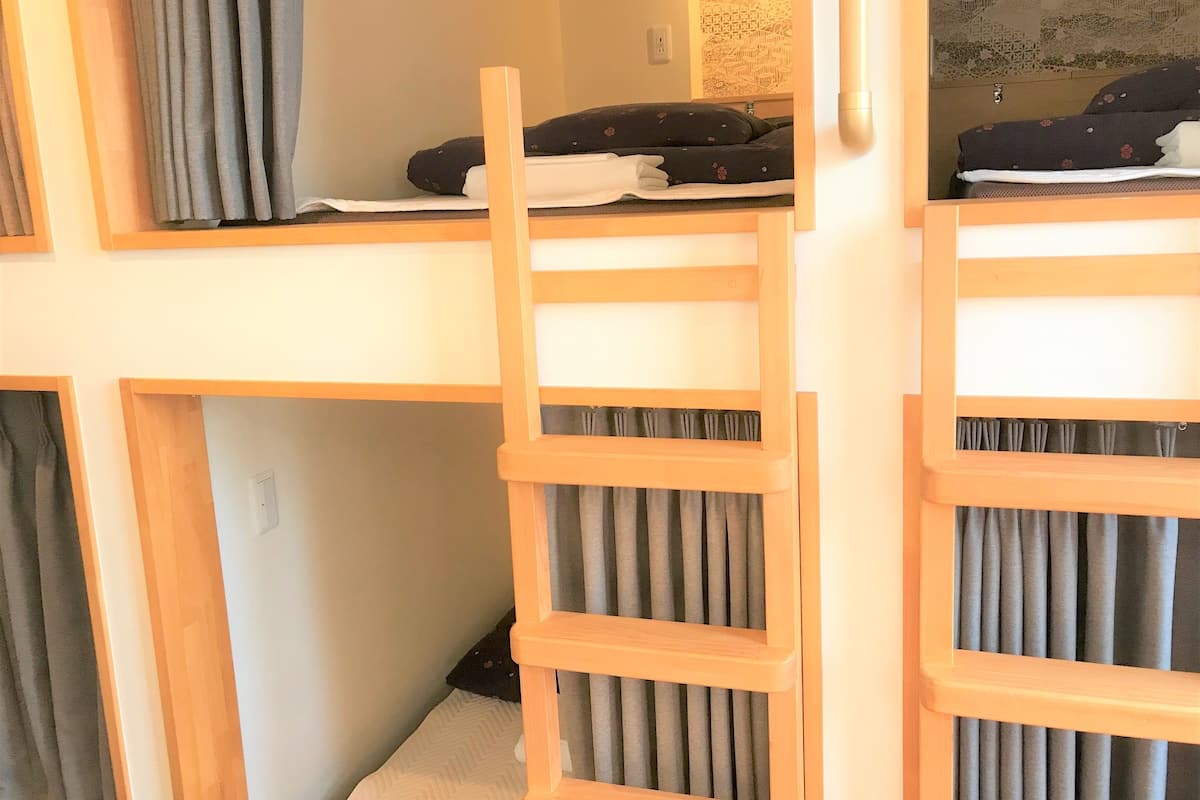Ein Stockbett mit Holzleiter, grauen Vorhängen und einer Wand mit Muster.