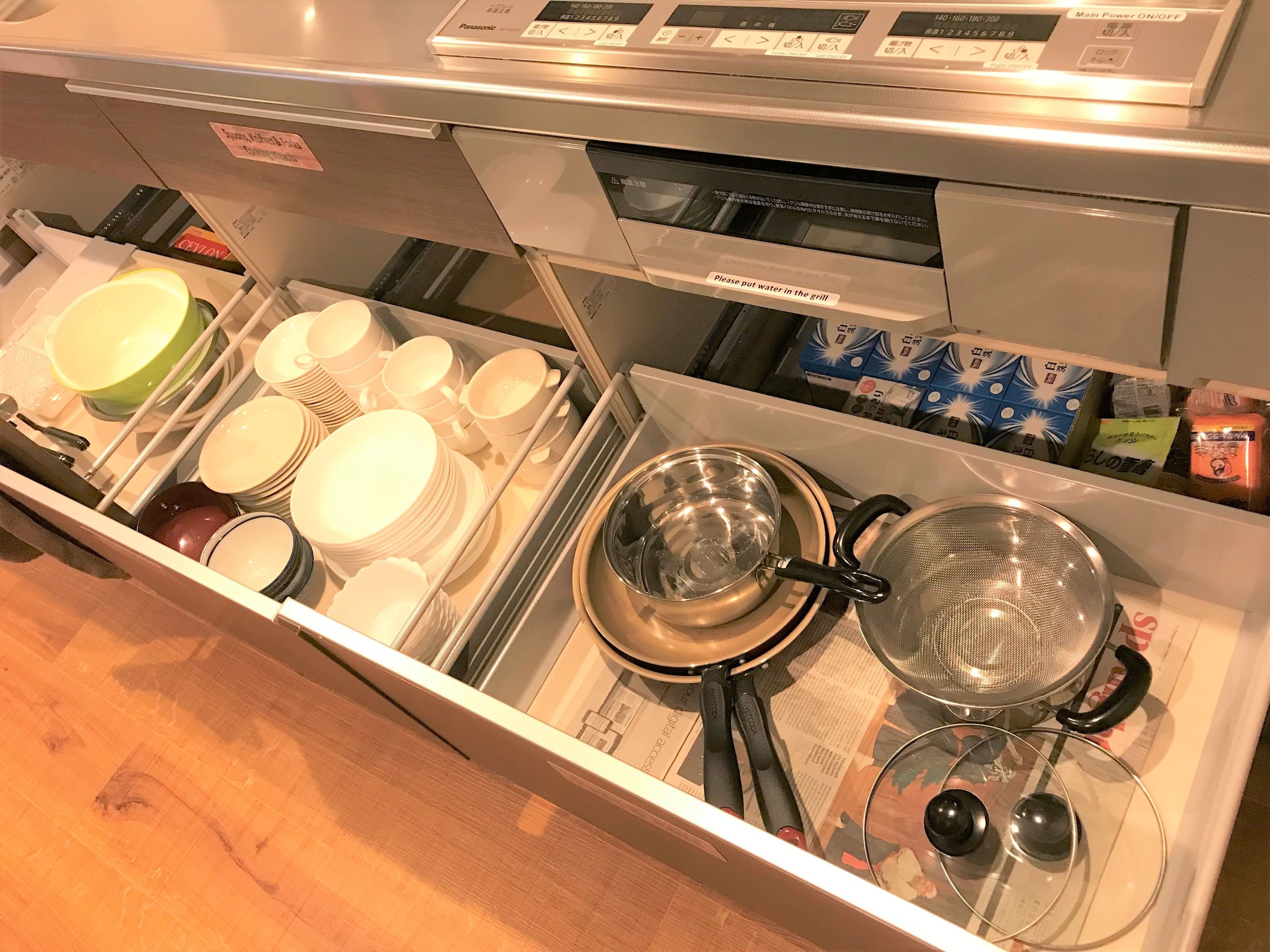 A kitchen drawer with stacked plates, bowls, and cooking utensils.
