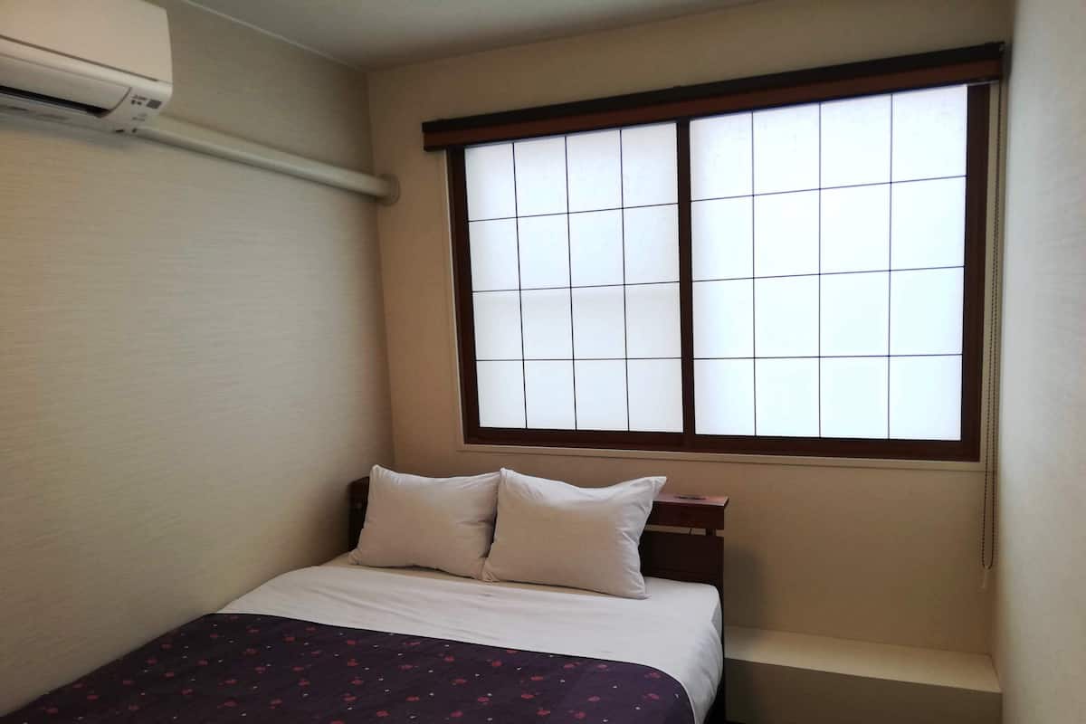 Ein Hotelzimmer mit einem Bett, einem Fenster mit Gittermuster und einem kleinen Nachttisch.