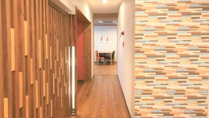 A hallway with wooden paneling on one side and a patterned wall on the other. There is a table and chairs in the distance, suggesting a dining area.