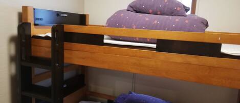 A bunk bed with a laptop on the top bunk, a window with a blind, and an air conditioning unit above.