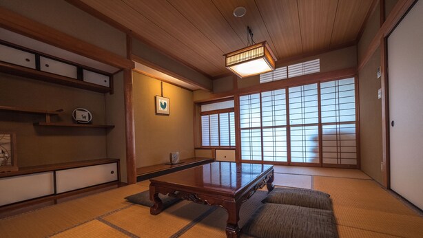 A traditional Japanese room with tatami flooring, a low wooden table, sliding shoji doors, and a ceiling light fixture.