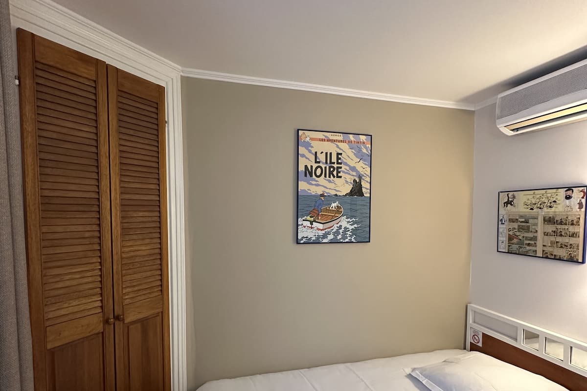 A hotel room with a bed, a wooden wardrobe, and a wall-mounted air conditioner.