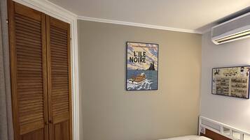 A hotel room with a bed, a wooden wardrobe, and a wall-mounted air conditioner.