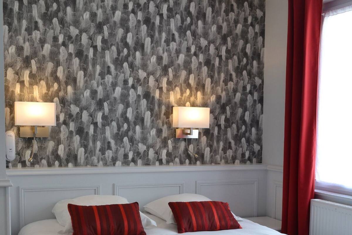 A hotel room with a large bed, two wall-mounted lamps, and a red curtain.