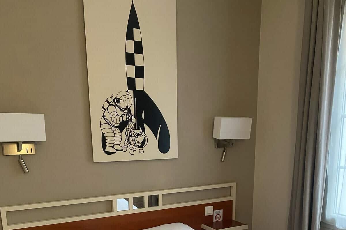 A hotel room with a large bed, two bedside lamps, a wall-mounted artwork, and a window with curtains.