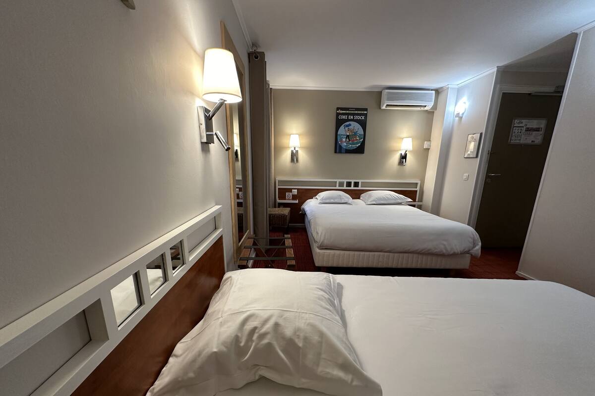 A hotel room with two beds, a mirror, a poster, and a door.