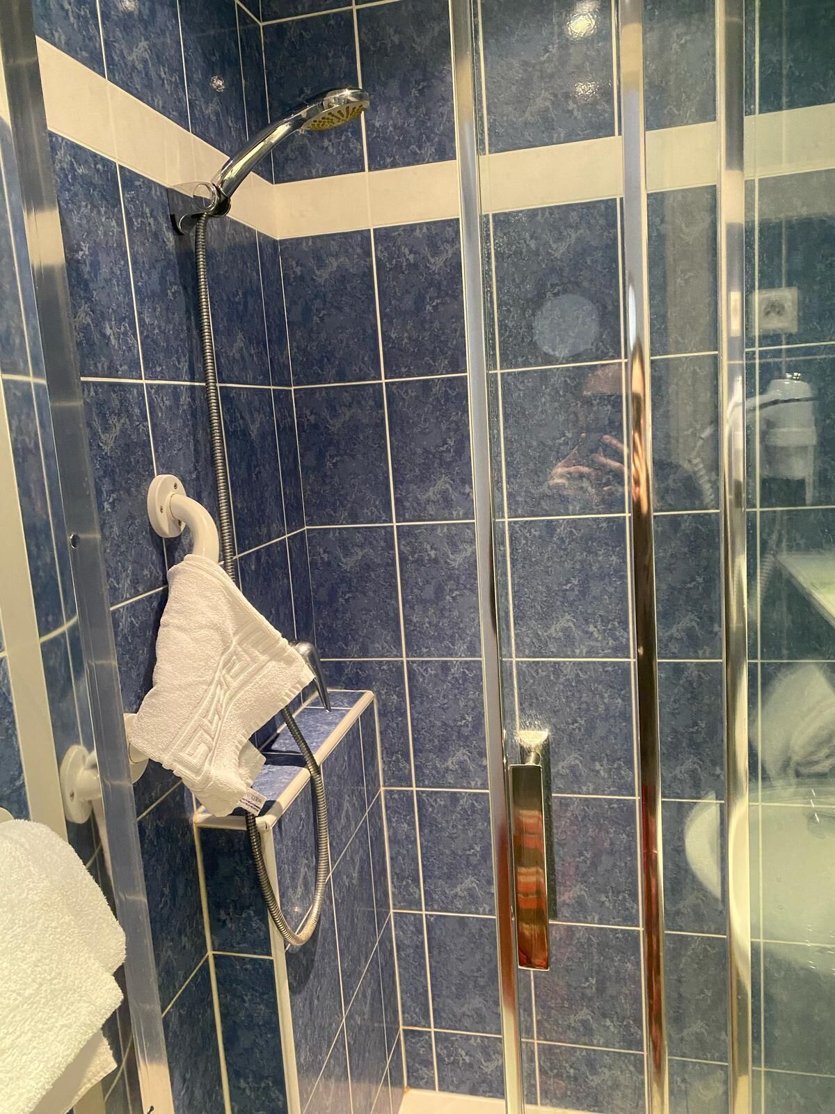 Ducha con puerta de cristal, cabezal de ducha de mano y toallero con una toalla blanca.