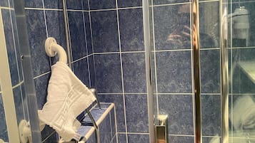 Ducha con puerta de cristal, cabezal de ducha de mano y toallero con una toalla blanca.