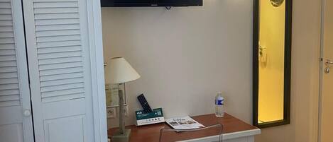 Una habitación de hotel con cama, escritorio con lámpara, televisión y espejo.