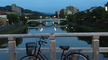 A bicycle parked by a calm river with a bridge in the background.