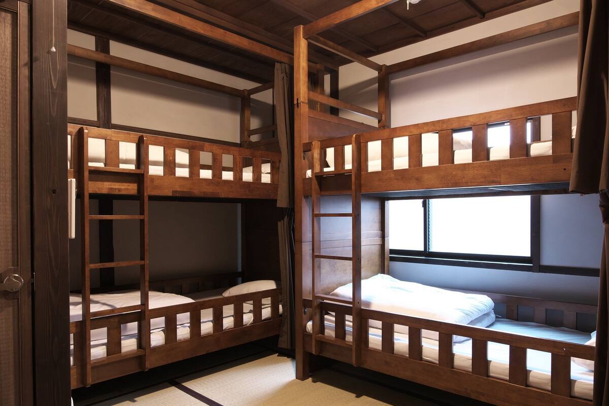 A traditional Japanese-style room with tatami flooring, wooden bunk beds, and a window providing natural light.