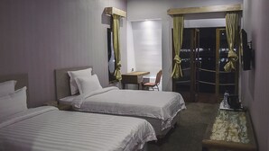 A hotel room with two beds, a small desk, a chair, and a view of the outside. - Kanaka Lake Villa (Batam)