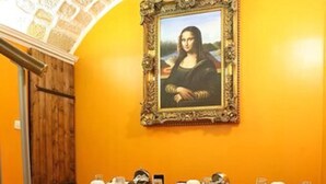 Uma área de refeições com uma mesa posta para quatro pessoas, um quadro grande emoldurado na parede e uma porta de madeira.