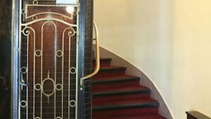Uma escadaria com degraus revestidos de carpete vermelho que levam a um portão de metal preto com detalhes ornamentados.
