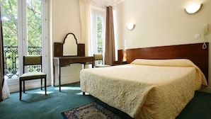Quarto de hotel com uma cama grande, uma escrivaninha com cadeira, uma janela com cortinas e uma varanda com cadeira.