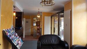 Um hall com um sofá de couro preto, um candelabro, um suporte para revistas e uma porta com a inscrição 'SORTIE'.