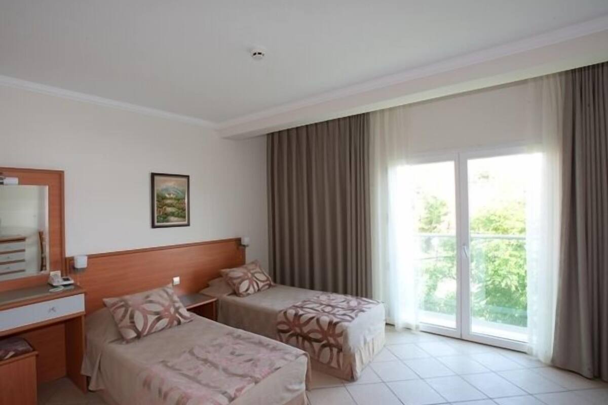 Habitación de hotel con dos camas, un escritorio, un espejo y un ventanal grande con cortinas.