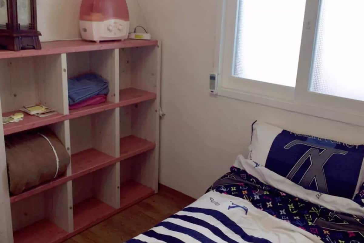 Une chambre à coucher avec un lit, une fenêtre et une étagère contenant divers objets.