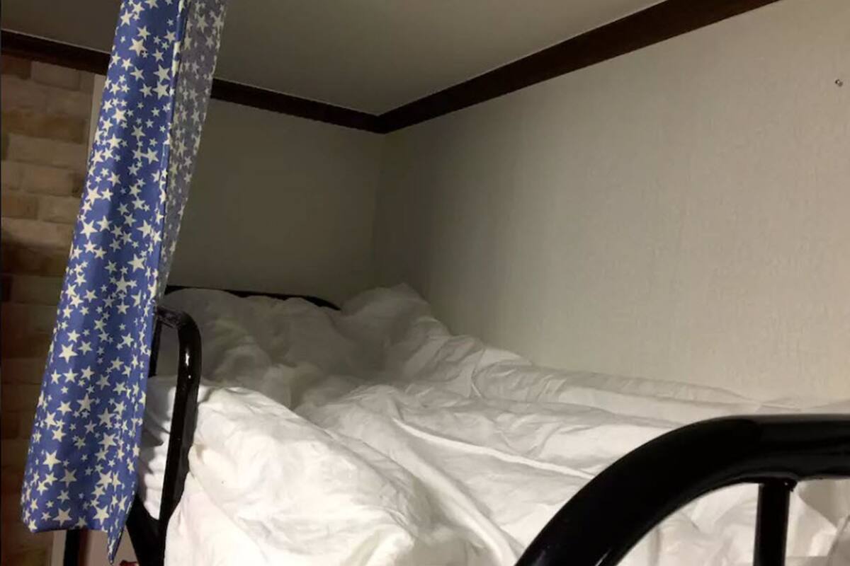 Une chambre avec un lit superposé, un rideau bleu orné d’étoiles et un mur blanc.