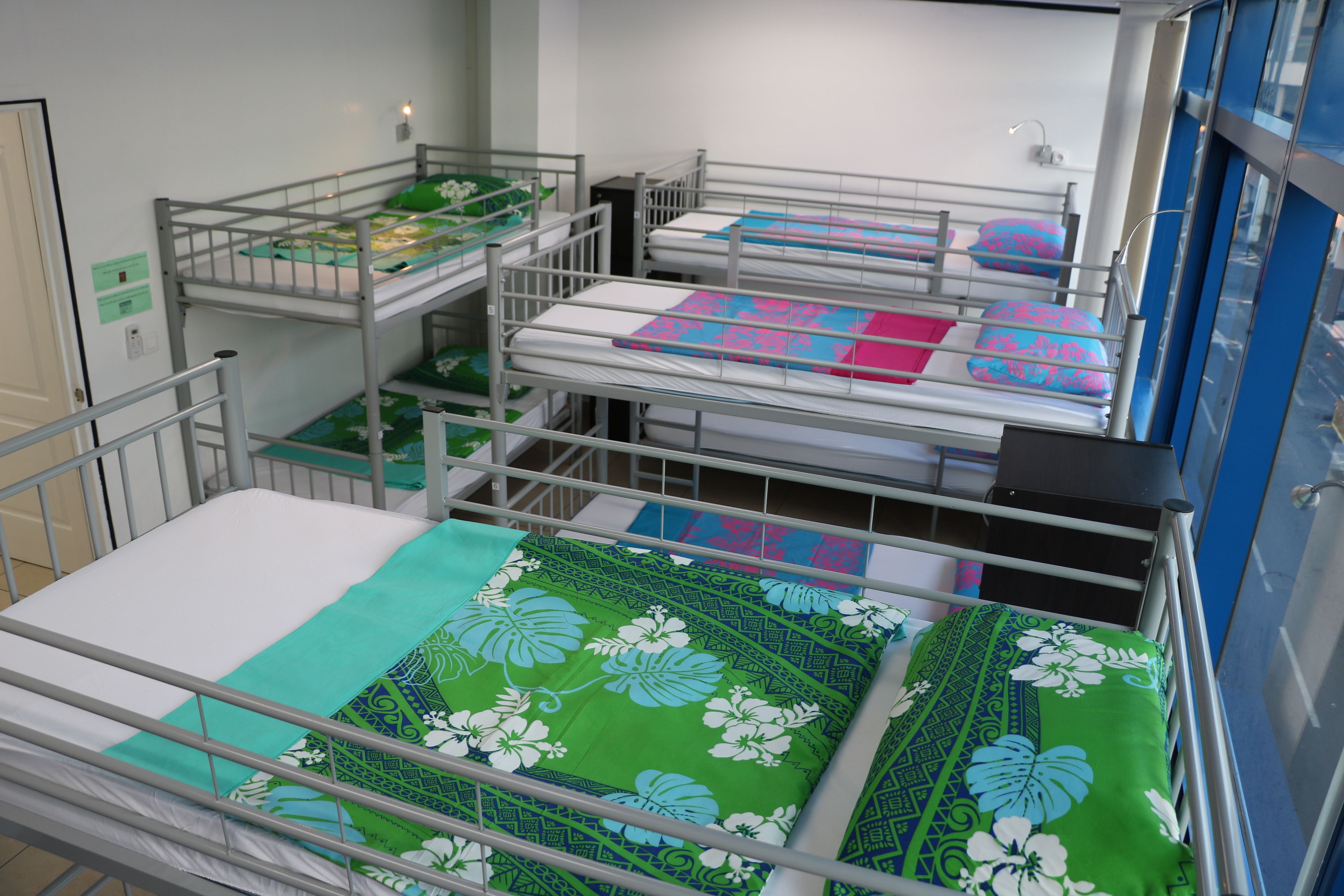 A hospital room with multiple beds, each with a green floral bedspread and a metal railing.