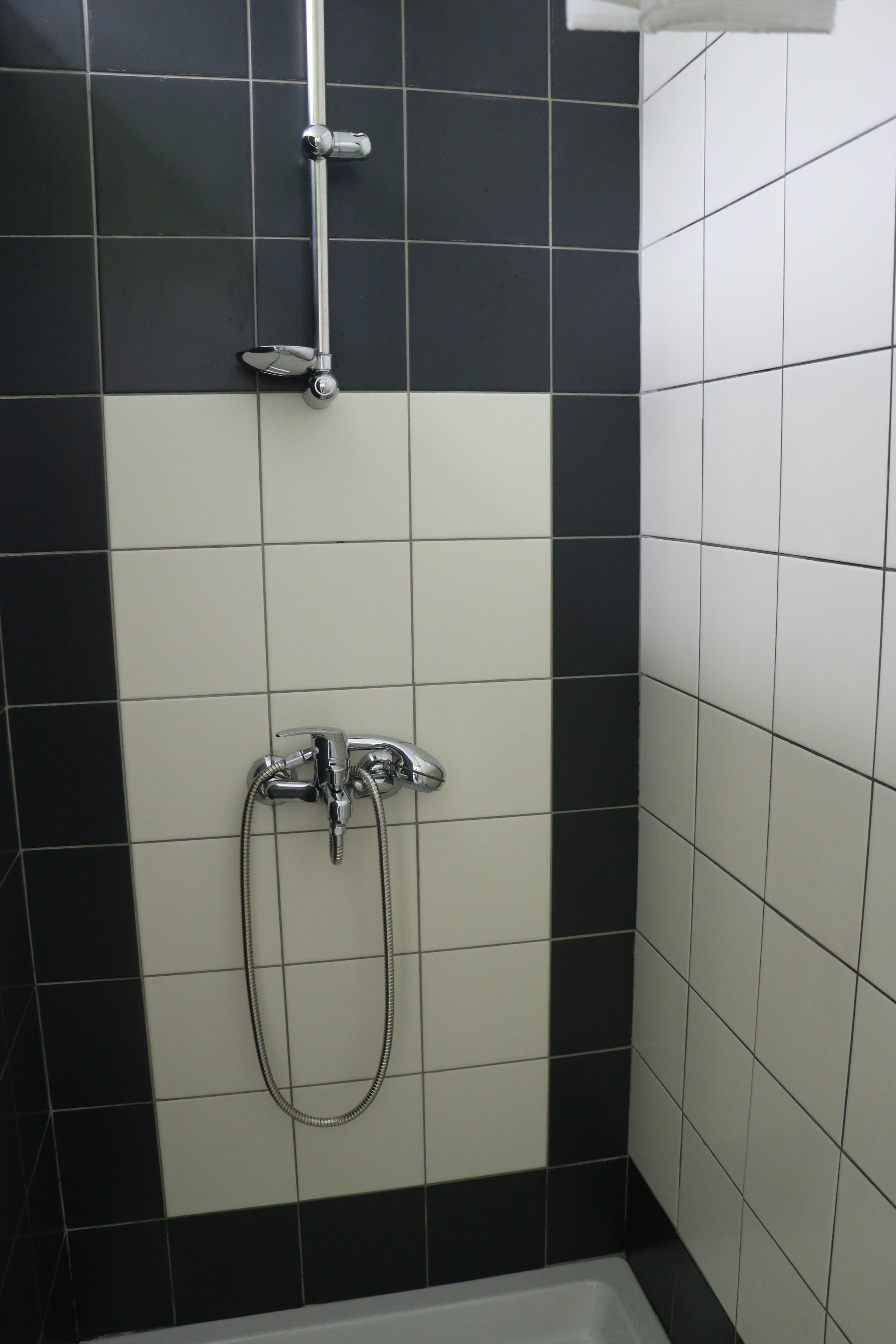 Zona de ducha con azulejos blanco y negro, un cabezal de ducha de mano y un grifo empotrado en la pared.