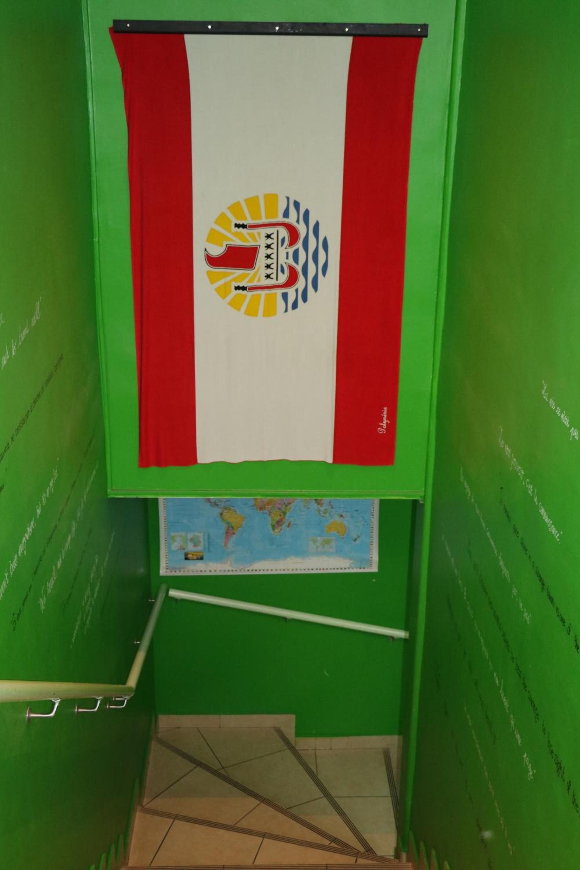 Una habitación con paredes verdes, una bandera roja y blanca con un logotipo, un mapa pequeño y una ventana que ofrece vistas al exterior.