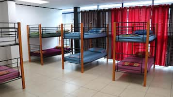 A dormitory room with bunk beds, a window with red curtains, and a tiled floor.