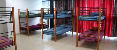 A dormitory room with bunk beds, a window with red curtains, and a tiled floor.